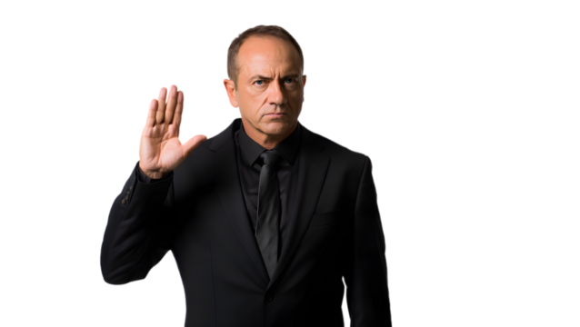 Serious man in black suit raises hand in gesture against dark background
