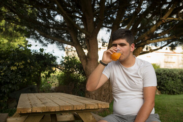 Fototapeta premium Adolescente a beber sumo de laranja natural num jardim á sombra do pinheiro manso.