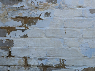 White paint peeling from a brick wall revealing red brick underneath. Decay and vintage texture.