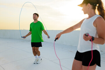 Two fitness enthusiasts jump rope together, enjoying an active workout on a rooftop during twilight