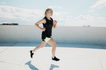 Dynamic woman enjoys running on a rooftop under a bright sky in a vibrant urban setting while...