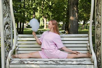 A girl does the splits on a bench, holding cotton candy in her hands