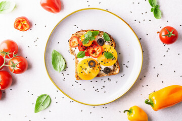 Bright homemade sandwiches with full grain toasts, cream cheese, juicy tomatoes, bell pepper, olives and aromatic herbs on light stone background top view. Healthy tasty breakfast idea.