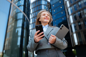 Business professional confidently engaging with devices outside modern skyscrapers