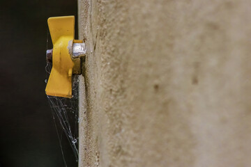 A yellow gas turn valve with spider webs on it, attached to the cement wall of a farm house in the eastern Andean mountains of central Colombia, near the town of Villa de Leyva.
