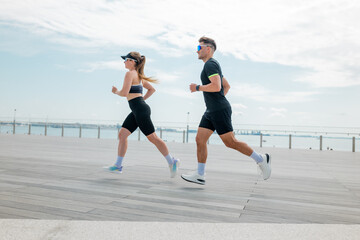 Dynamic duo jogs along the waterfront pathway, enjoying fitness and fresh air in a beautiful...