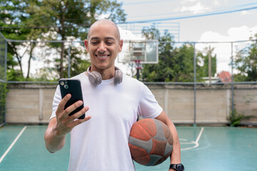 Latin man using smartphone on outdoor basketball court, urban sports fitness lifestyle