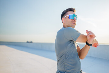 An enthusiastic young man performs stretches to warm up before going for a run on a rooftop that...