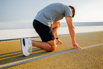Runner preparing for a sprint on a track, focusing on starting position and determination, as the...