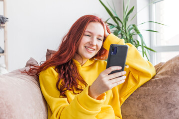 Smiling teenage girl sitting on couch and looking at phone screen