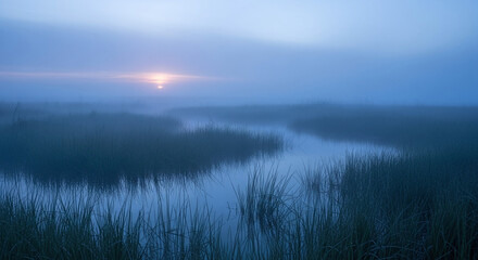 Misty morning sunrise over a serene marsh with calm water reflecting the sky