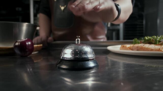 Chef rings the tabletop bell when a dish is ready in a restaurant kitchen. Close-up