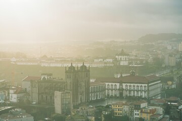 Historic buildings stand shrouded in mist in the city of Porto, Portugal. The soft morning sunlight illuminates the landscape, creating a hazy, ethereal atmosphere