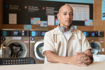 Bald Latin man sitting in laundromat with washing machines in background
