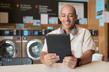 Latin man using digital tablet computer in laundromat with washing machines in background © Ranta Images