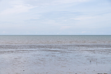 Calm shoreline under cloudy sky with low tide revealing wet sand and shallow water at a tranquil...