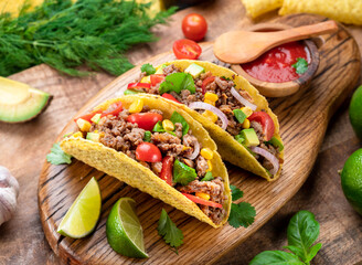 Mexican meat tacos or beef stuffed tortillas and lime slices near them on wooden serving board.