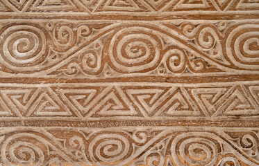 Complicated swirl and triangle patterns on an old wooden bench in pale brown colors