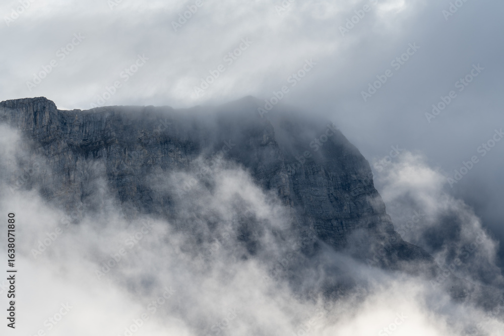 Wall mural prominent rocky mountains surrounded by mist and clouds and creating a rugged and magical setting