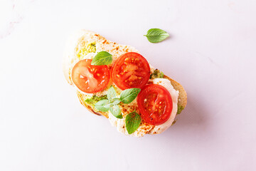 Fresh homemade caprese sandwich with avocado paste, mozzarella cheese, cherry tomatoes, fresh aromatic basil leaves and spicy hot oil top view. Healthy homemade food concept.