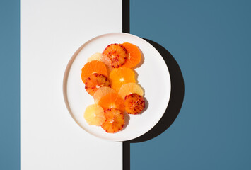 Surtido de rodajas de cítricos en un plato blanco sobre fondo azul y blanco. Vista superior