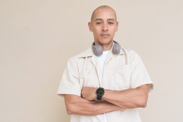 Bald Latin man in casual shirt with headphones around neck against beige background