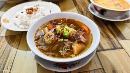 Delicious Soto Noodle Soup, indonesian traditional street food, consisting of yellow broth, beef, celery, vegetables, spring rolls, tomatoes, potatoes, noodles, and lime