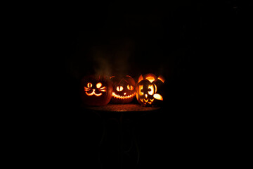 Three funny carved pumpkin faces light up at night for Halloween