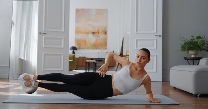 Fitness enthusiast performing side plank exercise on yoga mat in bright, modern living room