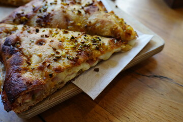 Close-up of sliced pizza with melted cheese and spices on wooden board, delicious Italian fast food, traditional baked snack for lunch, dinner, or takeaway. (