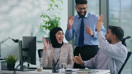 Excited Arabian Muslim business team celebrating success in office achieve goal looking at computer cheering smiling giving high five feeling happy teamwork motivation career partnership win teamwork