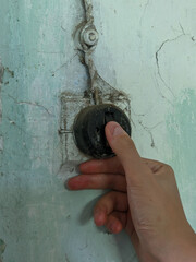 Hand reaching for a vintage light switch on a cracked and dirty wall in an old rural home.