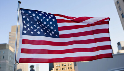 Fototapeta premium American flag waving on a pole outside a building showing stars and stripes in the wind against a clear sky