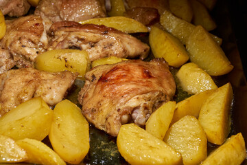 Oven-baked chicken pieces with potato slices and seasoning mixture. Close-up.