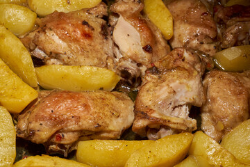Oven-baked chicken pieces with potato slices and seasoning mixture. Close-up.