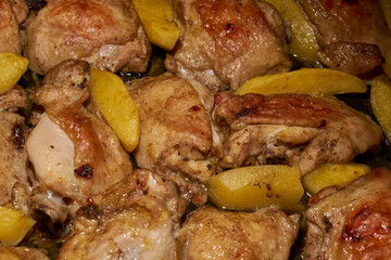 Oven-baked chicken pieces with potato slices and seasoning mixture. Close-up.