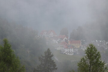 Foggy view of a small village with red-roofed houses surrounded by trees and hills