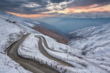 Winding mountain road through snow-covered terrain at sunrise