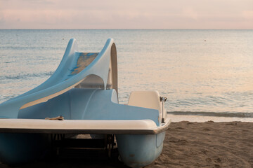 A pedal boat with a slide for children on the seashore, ready for a fun day of activities. The calm sea and sandy beach create a perfect summer scene.