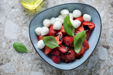 Strawberry caprese with mini mozzarella and basil in a blue bowl, horizontal shot on a brown...