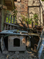 Disorganized rural yard with broken wooden furniture, doghouse, and scattered planks. Abandoned and rustic setting.