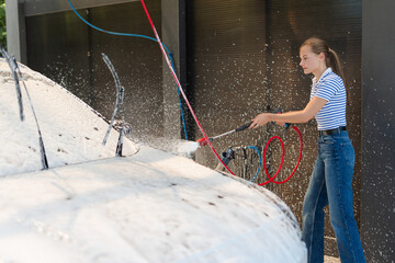 Young woman washing car with high pressure washer at self-service car wash