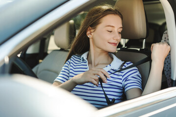 Young beautiful woman fastening seat belt while driving car