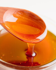 Close-up of golden honey dripping from a wooden spoon into a glass bowl. The rich amber color and...