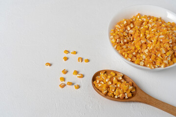 Loose corn kernels arranged on a wooden spoon and in a white ceramic bowl, on a white table.