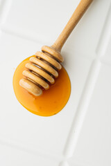 Close-up of golden honey with a wooden honey dipper on a white textured surface. The rich amber...
