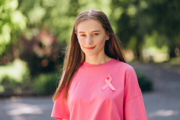Young woman wearing pink t-shirt with pink ribbon supporting breast cancer awareness in park