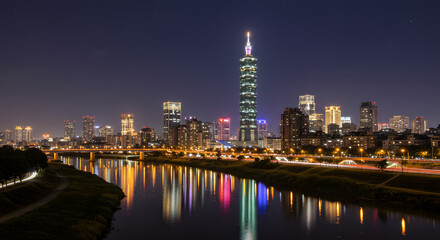 Naklejka premium Illuminated Taipei city skyline at night featuring the iconic Taipei 101 tower with vibrant light reflections on the Keelung River.