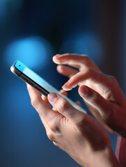 Close up of hands using a modern smartphone for communication and entertainment against a blue background showcasing mobile technology and connectivity