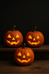 Obraz premium Three Glowing Jack-o'-Lantern Pumpkins on Wooden Table with Black Background, Halloween Decoration 